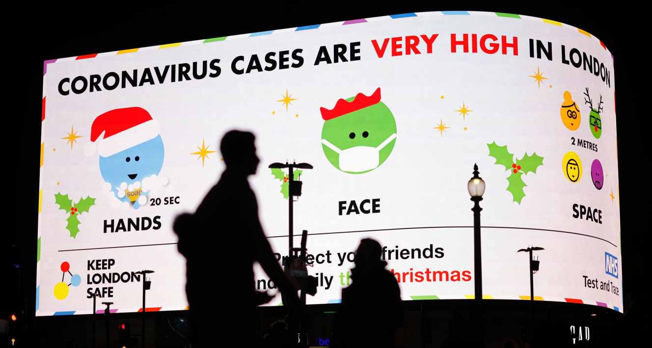 Des piétons passent devant un panneau d’information sur le Covid-19 avertissant que « le nombre de contaminations par le coronavirus est très élevé à Londres », à Piccadilly Circus, à Londres, le 19 décembre 2020.
